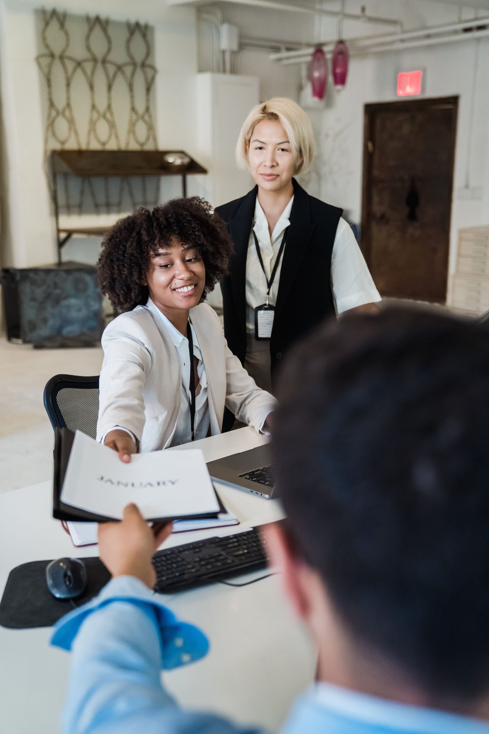 Une jeune femme souriante tend un document à un client vu de dos.